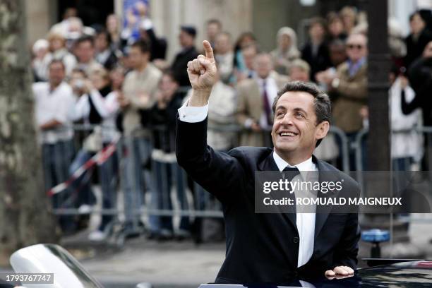 French President Nicolas Sarkozy waves from his car as he is driven up the Champs Elysees avenue in Paris in an open-top car, escorted by the mounted...