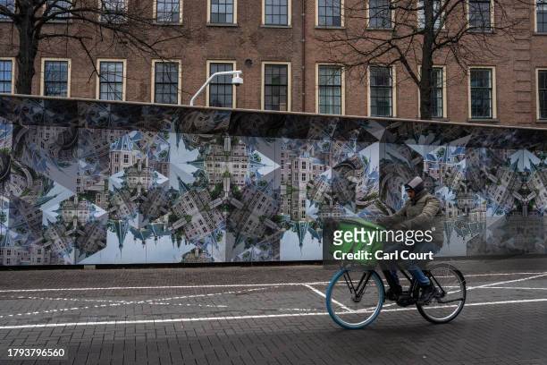 Man cycles past Martin Escher-inspired pictures of the Dutch parliament on hoarding surrounding a part of the parliament building that is being...