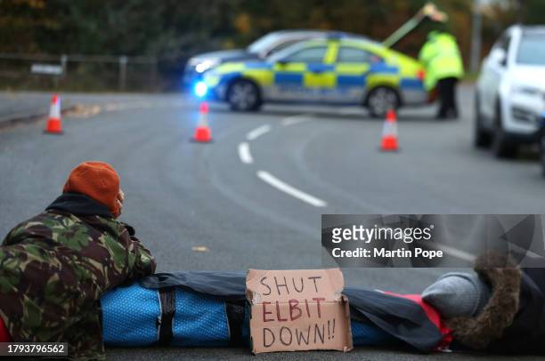 Two activists lay on the ground attached through a lock-on, blocking the road to traffic in Meridian East with a sign saying 'Shut Elbit Down' on...