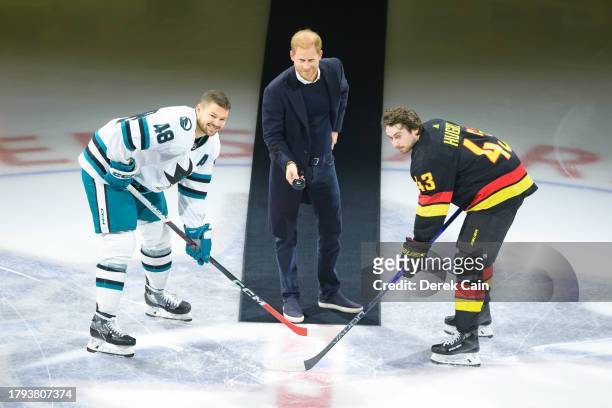 Prince Harry, The Duke of Sussex drops the puck during a ceremonial face-off with Quinn Hughes of the Vancouver Canucks and Tomas Hertl of the San...