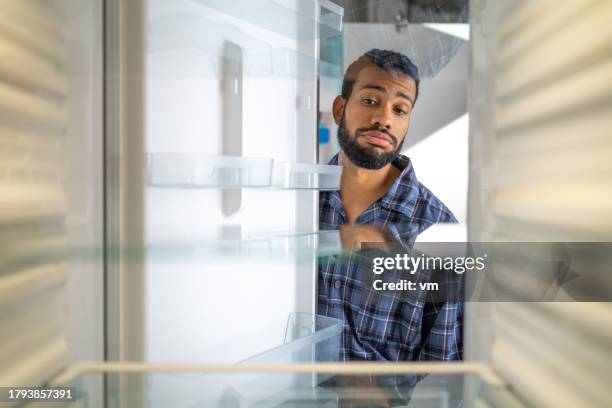 junger schwarzer mann schaut in einen leeren kühlschrank - kühlschrank leer stock-fotos und bilder