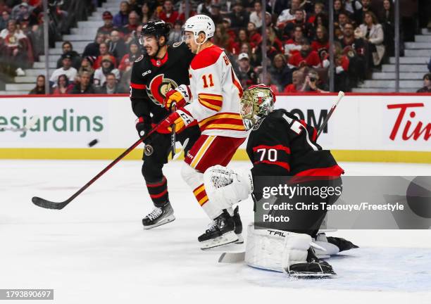 Mikael Backlund of the Calgary Flames battles with Travis Hamonic of the Ottawa Senators as his teammate Joonas Korpisalo tracks the puck at Canadian...