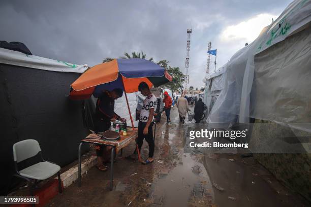 Palestinian man provides food on the side of a waterlogged alleyway between shelters at a camp, operated by the United Nations Relief and Works...