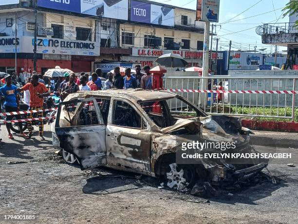 People look on at the a burnt out remains of a car in Monrovia on November 21 that rammed into a crowd of United party supporters as they celebrated...