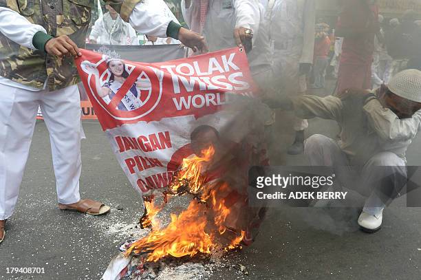 Indonesian Muslim protesters burn a banner featuring Miss World 2012 Yu Wenxia from China reading "Reject Miss World" during a protest in Jakarta on...