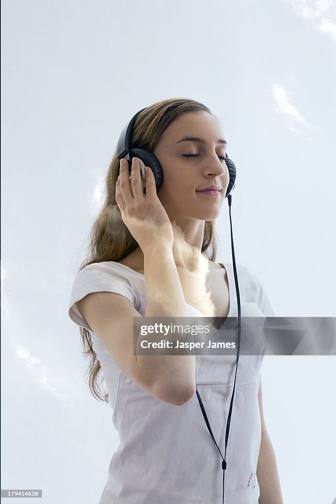 Composite of woman listening to headphones and sky