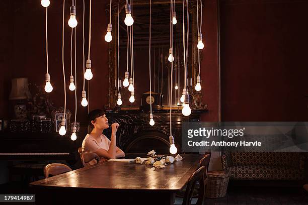 woman sitting at table with hanging lightbulbs - creatividad fotografías e imágenes de stock