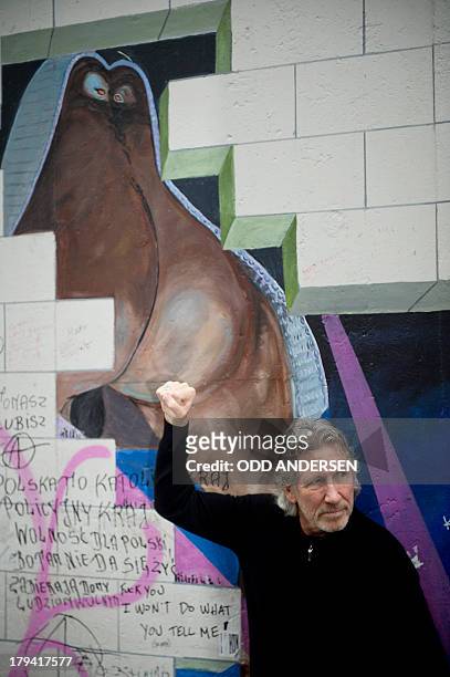 British musician Roger Waters clenches his fist as he poses for a picture next to art work from Pink Floyd's The Wall on the remains of the Berlin...