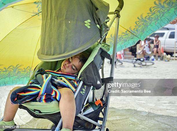 Lori Pirone and her partner Alejando Otero use an oversized umbrella to shade their 18-month-old from the sun August 26, 2013 at Burning Man. Burning...