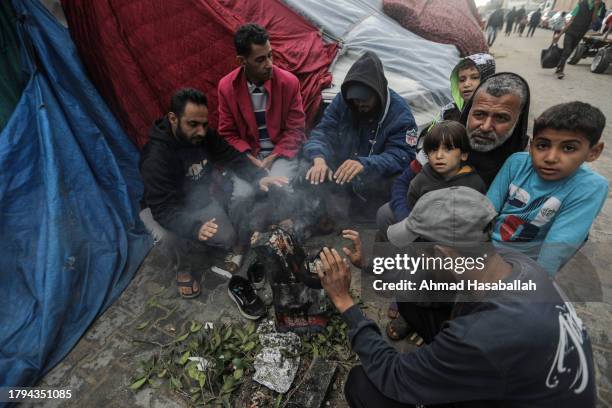 Displaced Palestinians sit in front of their tent, by a lit fire, and inspect the damage caused by rain on November 15, 2023 in Khan Yunis, Gaza. On...