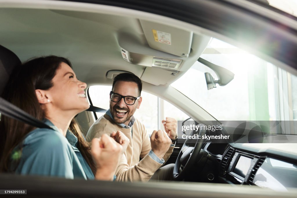 Happy couple celebrating their success inside of a car at showroom.
