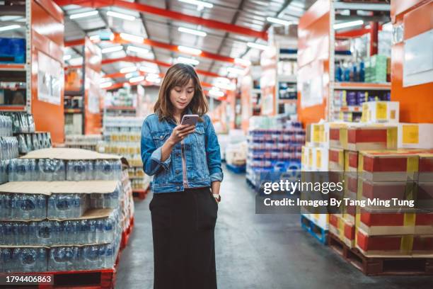 young female small business owner looking at the shopping list on her smartphone while shopping for groceries for her shop in wholesale store - liet stock pictures, royalty-free photos & images