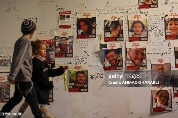 Children walk past portraits of Israeli hostages posted on a wall in Tel Aviv on November 21 demanding the release of Israelis held in Gaza since the...