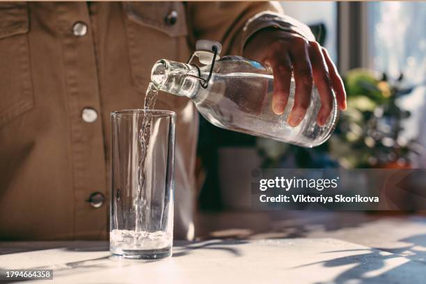 close up of woman pouring fresh water into glass from jug at home. attractive girl drinking water on domestic kitchen. young woman holding glass of water with lemon on kitchen in slow motion - girl filling water glass stock pictures, royalty-free photos & images