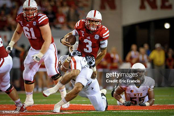 Quarterback Taylor Martinez of the Nebraska Cornhuskers runs through the grip of linebacker Sonny Puletasi of the Wyoming Cowboys during their game...