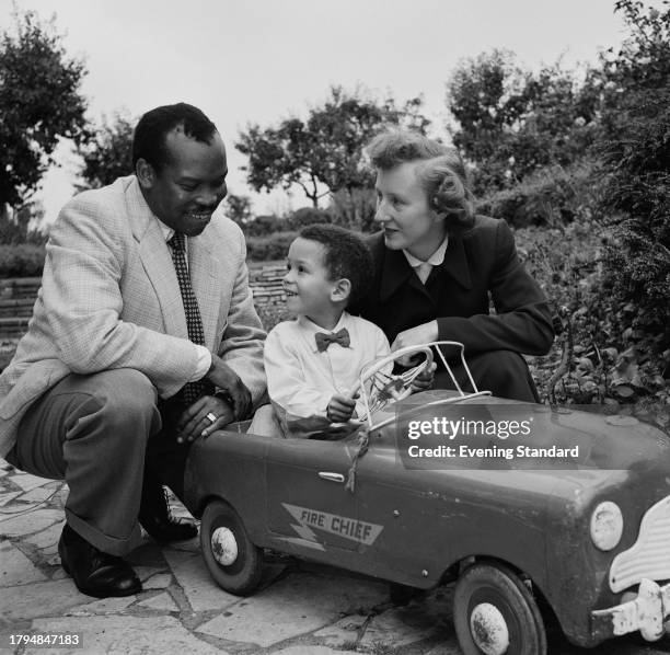 Bechuanaland Protectorate politician Seretse Khama crouching beside his son Ian Khama seated in a toy car, and wife Ruth Williams Khama , September...