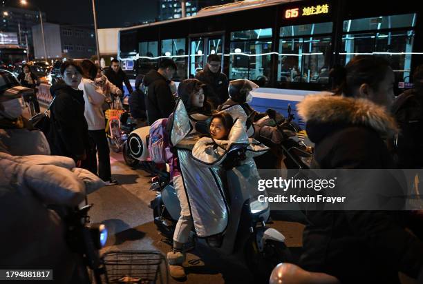 Girl looks up at her mother as she sits on her scooter while waiting with others to cross at an intersection during rush hour on November 15, 2023 in...