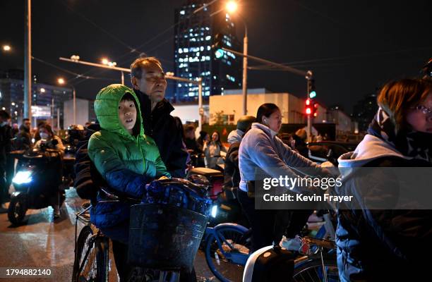 Boy and a man sit on their bicycle while waiting with others to cross at an intersection during rush hour on November 15, 2023 in Beijing, China....