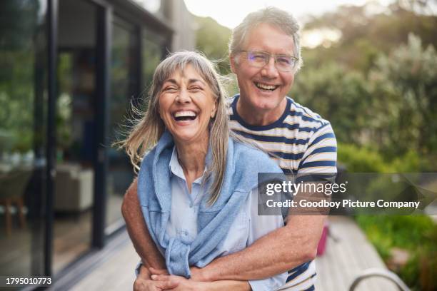 mature couple standing arm in arm and laughing outside in summer - sunny backyard stock pictures, royalty-free photos & images