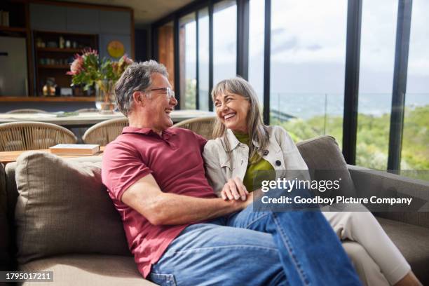 mature couple sitting on their living room sofa and laughing together - financial freedom stock pictures, royalty-free photos & images