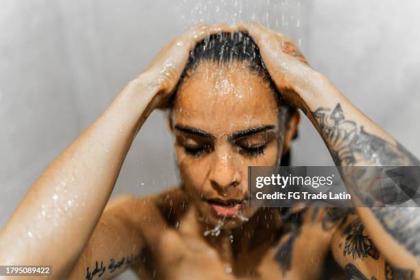 mid adult woman taking a shower in the bathroom - woman in shower tattoo stock pictures, royalty-free photos & images