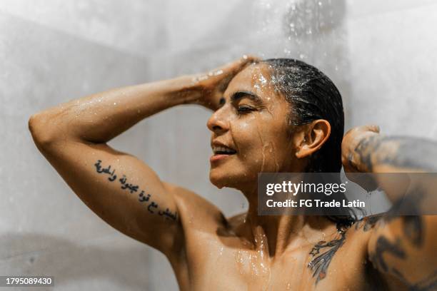 mid adult woman taking a shower in the bathroom - woman in shower tattoo stock pictures, royalty-free photos & images