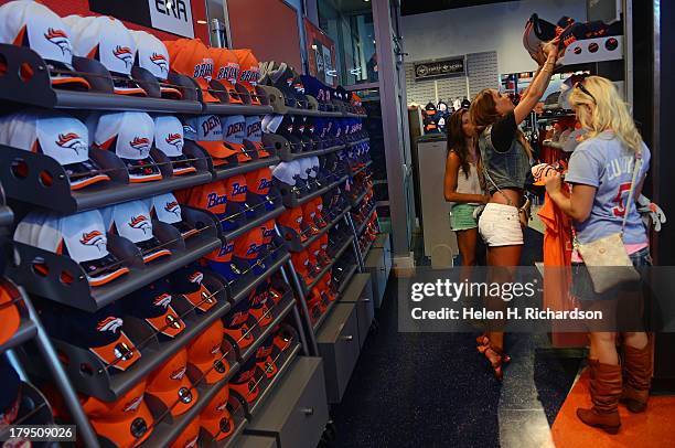 Kerri Stern stands on her tippy toes to reach a Broncos' hat to try on with her friends Danielle Glucky, right, and Toni Damico, in green shorts, at...