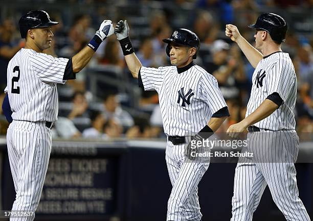 Derek Jeter of the New York Yankees congratulates teammates Ichiro Suzuki and Lyle Overbay after the two scored on a triple by Brett Gardner during...