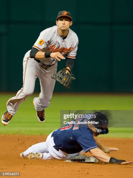 Second baseman Ryan Flaherty of the Baltimore Orioles jumps over Matt Carson of the Cleveland Indians after throwing to first for the double play...