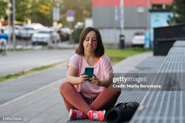 sad woman wearing sports clothing sitting with legs crossed and holding smart phone. - modern zagreb stock pictures, royalty-free photos & images