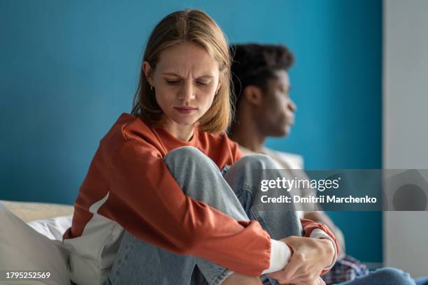 diverse couple experiences conflict sitting on bed. sad offended girl lowered head in frustration. - disgust stock pictures, royalty-free photos & images