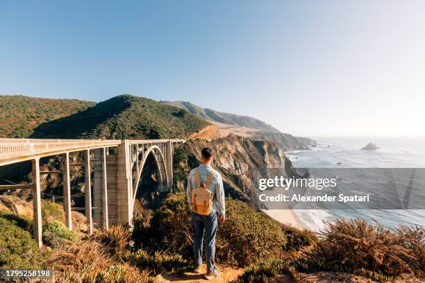 man with backpack exploring big sur near bixby bridge, california, usa - big sur stock-fotos und bilder