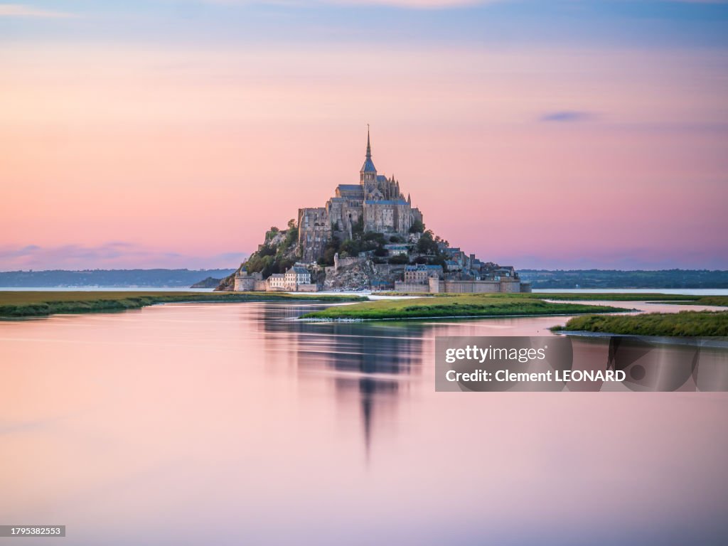 Distant view of the Mont Saint-Michel (Mont-Saint-Michel) reflecting in the sea at sunset during high tide, Manche, Normandie (Normandy), Western France.