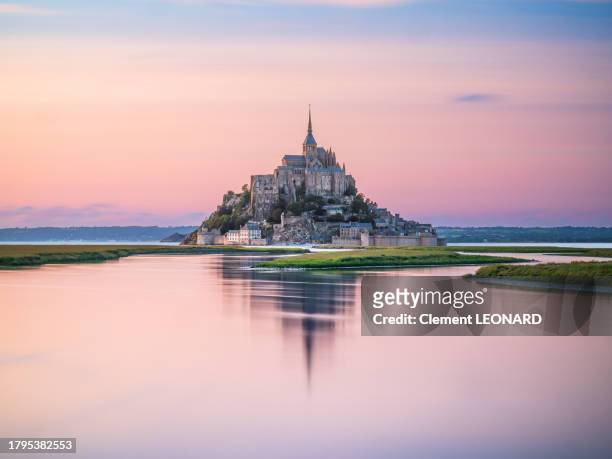 distant view of the mont saint-michel (mont-saint-michel) reflecting in the sea at sunset during high tide, manche, normandie (normandy), western france. - mont saint michel stock pictures, royalty-free photos & images