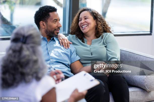 mittlere erwachsene frau lächelt und lacht, während sie ihrem ehemann zuhört - eheberatung stock-fotos und bilder