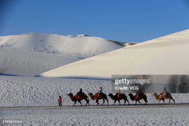 Tourists ride camels at Mingsha Mountain and Crescent Spring scenic spot after a snowfall on November 15, 2023 in Dunhuang, Jiuquan City, Gansu...