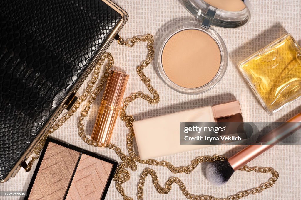 Set of Black Clutch Bag and Cosmetic Make-up Products for a woman on beige colour background.