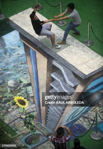 Two men pose by the work of British artist Julian Beever, specialized in pavement drawings, wall murals and realistic paintings, made in a shopping...