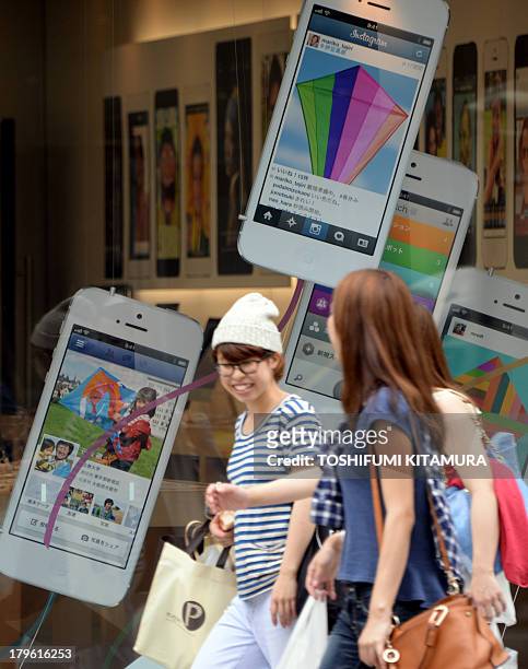 Pedestrians walk past advertisements for the iPhone 5 at the Apple store in central Tokyo on September 6, 2013. Japan's top mobile carrier NTT DoCoMo...