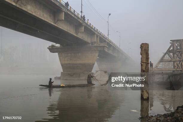 Fishermen are catching fish as labourers are dismantling an old damaged bridge over the Jehlum River on a foggy day in Sopore District, Baramulla,...