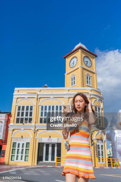 asiatische frau der generation z mit smartphone, während sie auf reisen den charme der altstadt von phuket erkundet und sich jederzeit und überall mit sozialen medien verbindet. junge frau interagiert mit geräten. konnektivität: lebensstile mit geräte - phuket old town stock-fotos und bilder