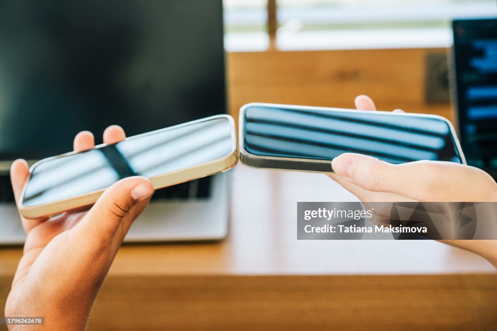 Two phones in women’s hands transmit data to each other via bluetooth. Close-up.