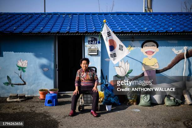 An elderly woman rests her eyes while sitting in front of a mural outside a property in Dongducheon, Gyeonggi Province, about 38 kilometers north of...