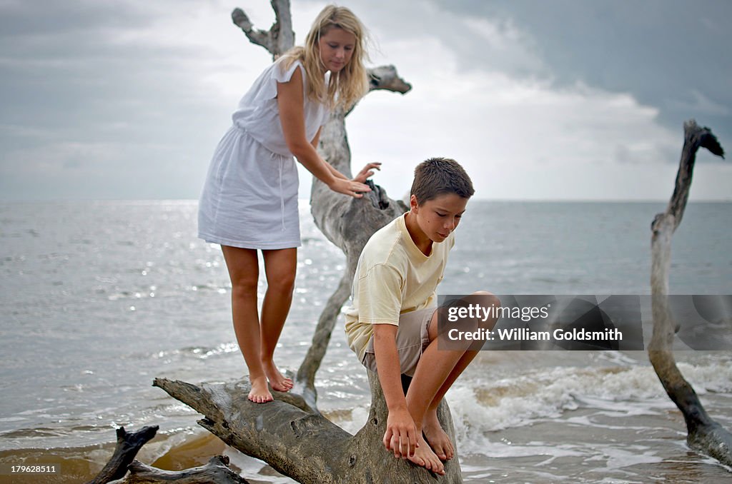 Brother and Sister Climb Large Drift Wood on Beach