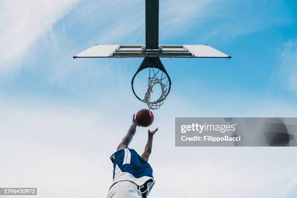 vista ad angolo basso di un giovane adulto che segna un gol in un campo da basket - fare canestro foto e immagini stock