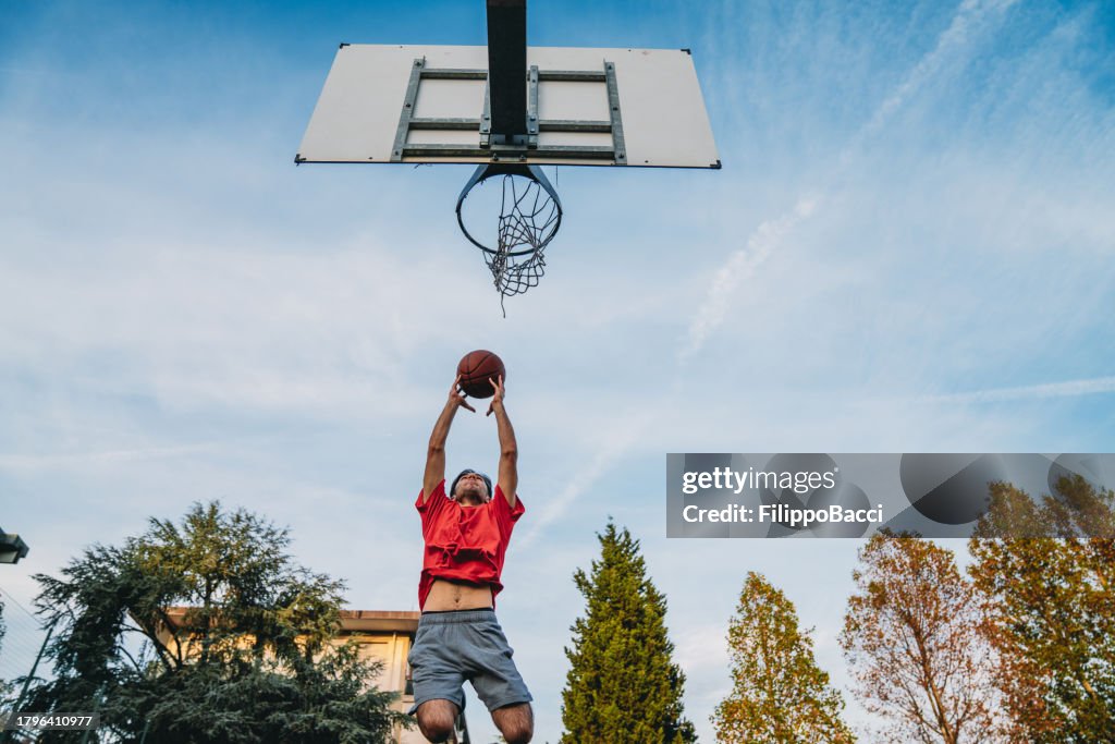 Vista ad angolo basso di un giovane adulto che segna un gol in un campo da basket