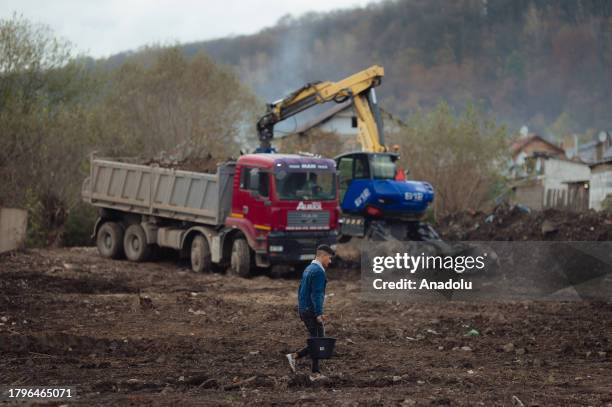 Young man carries a bucket of freshwater from the nearby river Bodva as workers with heavy machinery remove tons of accumulated waste by the...