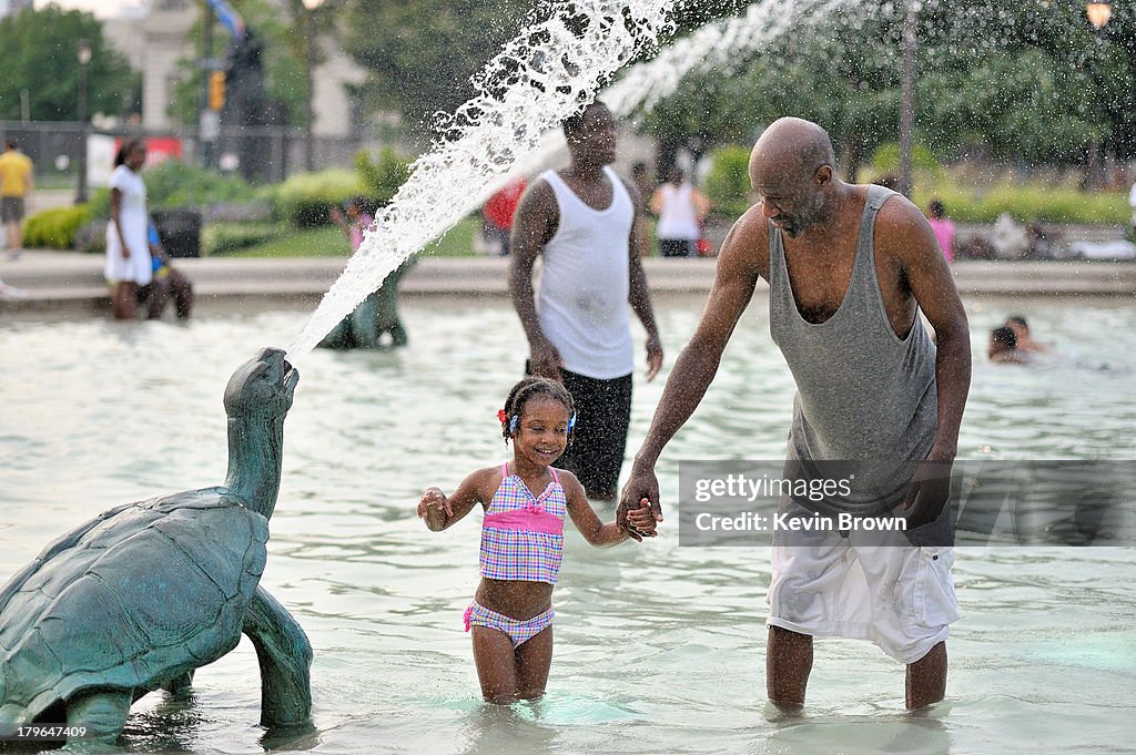 Grandfather and grandchild cool off in fountain.