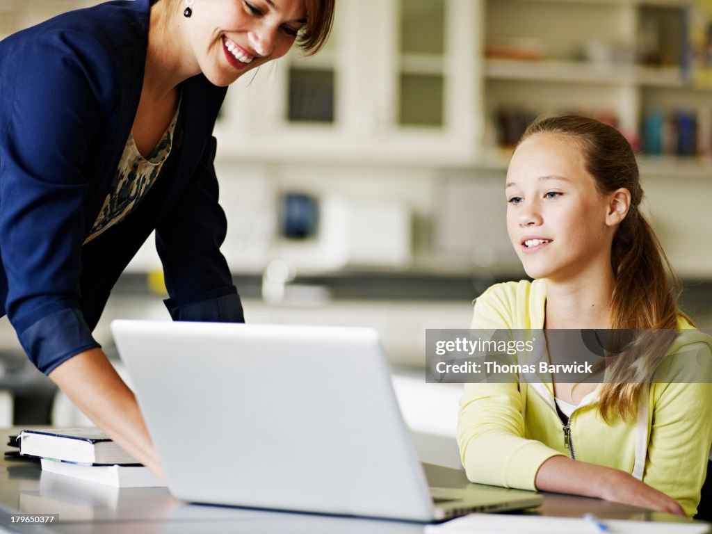 Teacher helping young student working on laptop