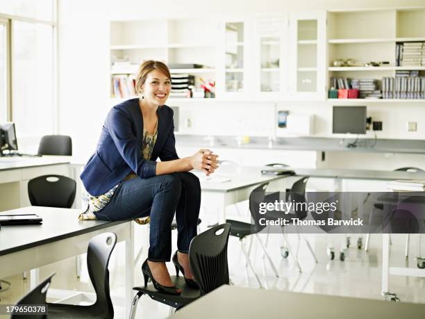 smiling teacher sitting on desk in classroom - smart shoes stock pictures, royalty-free photos & images